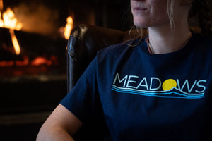 Person sitting in front of fireplace wearing a Meadows tshirt