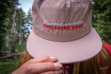 Pink cap with 'Mt. Hood Meadows Avalanche Dogs' text held by a person in a forest setting