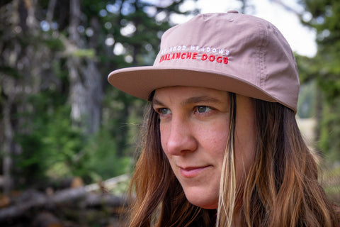 Person wearing a pink cap with 'Mt. Hood Meadows Avalanche dogs' embroidered text in a forest setting