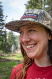 Person wearing a camouflage cap with a patch logo in a forest setting