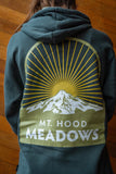 Person standing in front of a wooden wall wearing a hoodie featuring a Mt. Hood Meadows print.