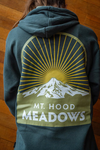 Person standing in front of a wooden wall wearing a hoodie featuring a Mt. Hood Meadows print.