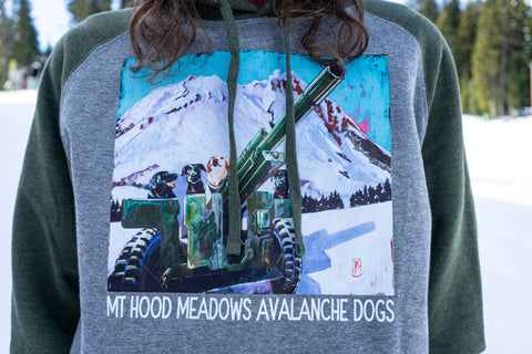 Person wearing a sweatshirt with a graphic design of a snow-covered mountain and avalanche dogs, set against a snowy landscape.