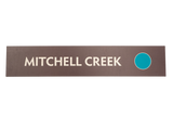 Rectangular brown sign with 'Mitchell Creek' text and a green circle icon