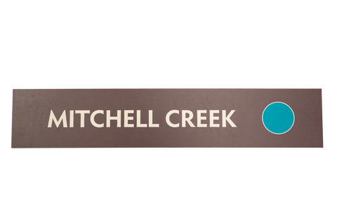 Rectangular brown sign with 'Mitchell Creek' text and a green circle icon