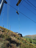 Person ziplining down a hill with a clear blue sky and mountains in the background