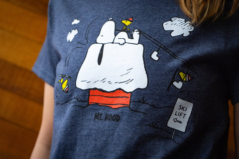 A persons torso standing against a wooden wall. They are wearing a shirt with a ski lift print on it.