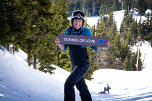 A person standing on a ski slope holding a trail sign