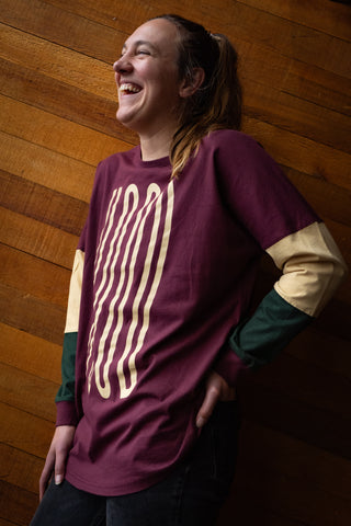 Person standing in front of a wooden wall wearing a Maroon crew shirt with beige text on the front.